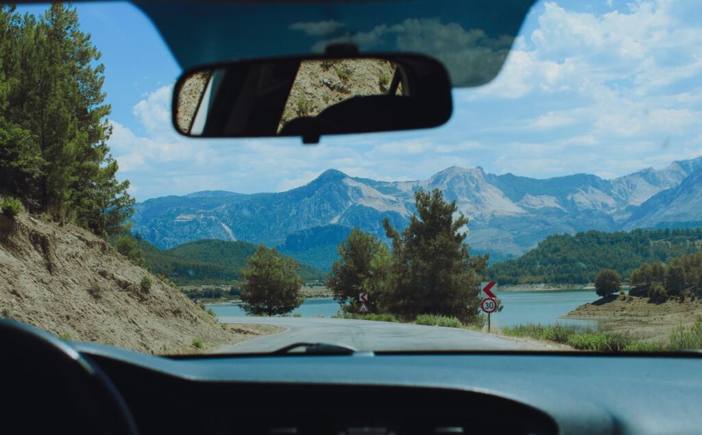 View through a car windshield of a mountain road beside a lake