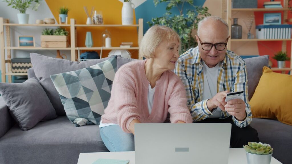 Older couple on a sofa checking a payment card while shopping online on a laptop