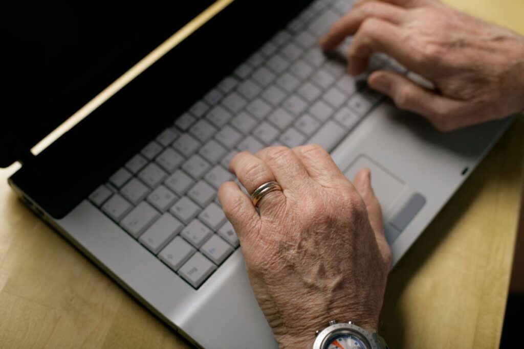 Close-up of an older person typing on a laptop keyboard