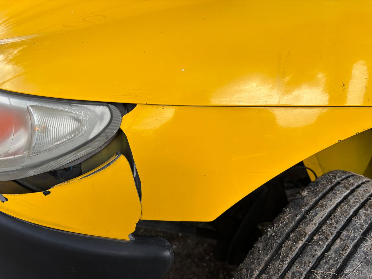 Close-up of a dented front bumper and headlight on a yellow car