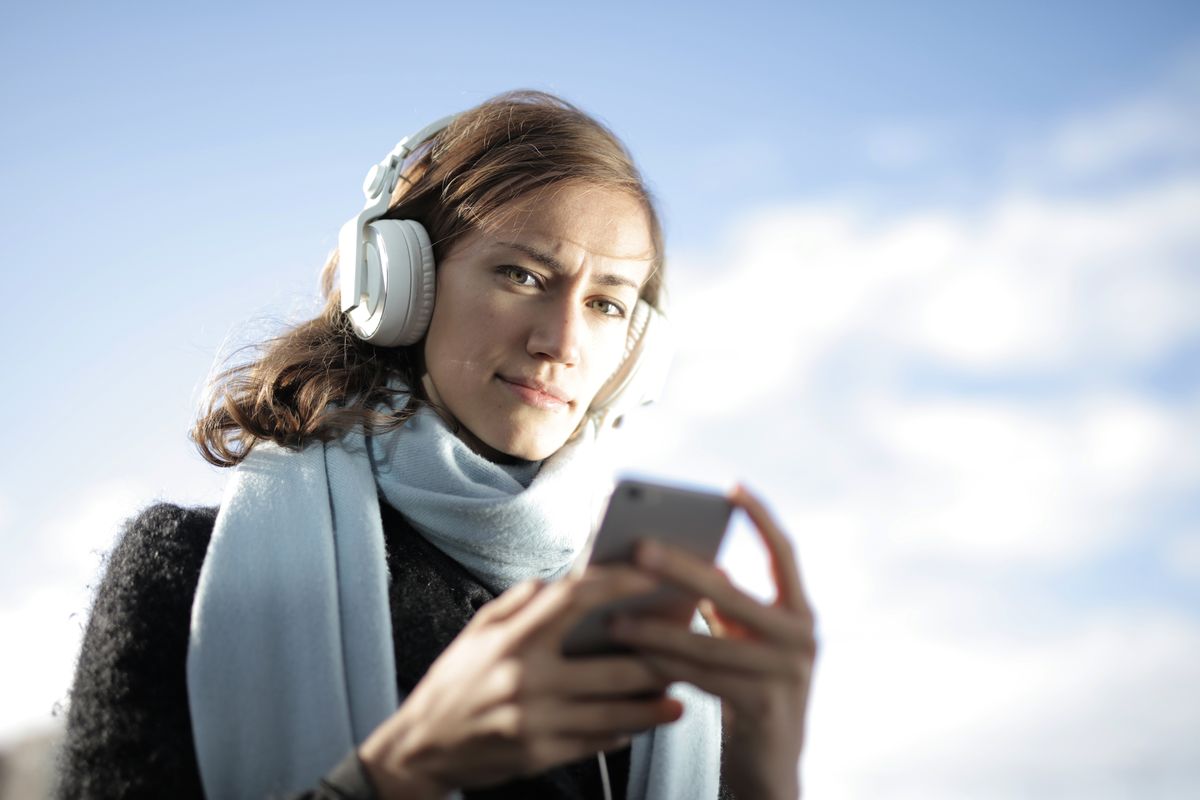 Woman with headphones choosing an album on her phone outdoors