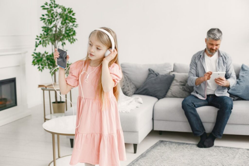 Girl listening to music on headphones while her father relaxes in the living room