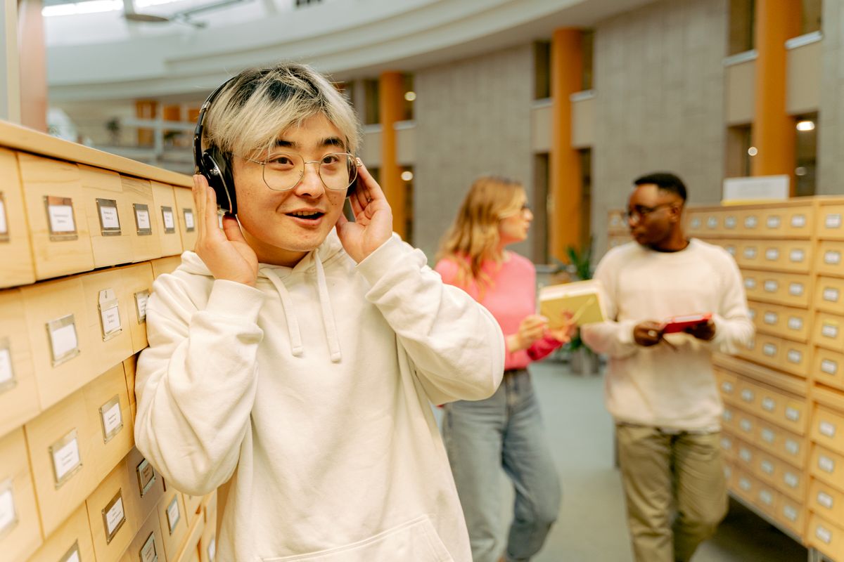 Student smiling while listening to music on headphones in a library