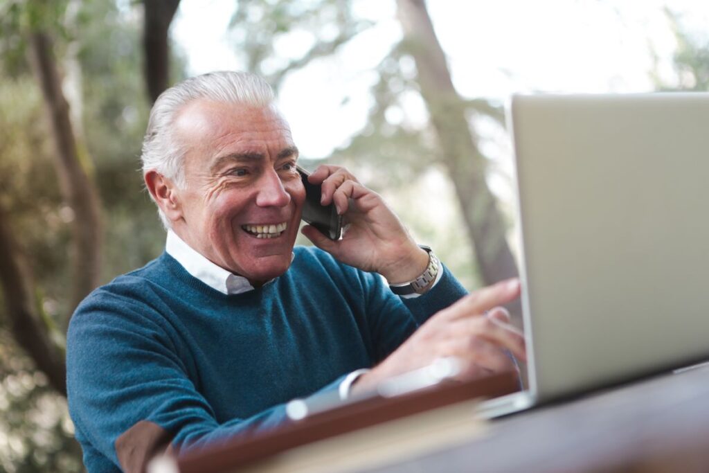 Smiling older man talking on his phone while working on a laptop