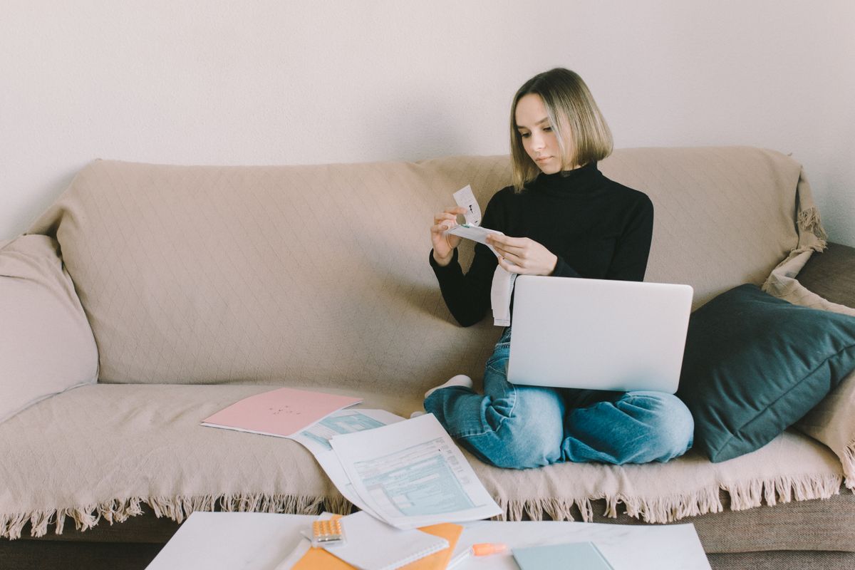 Woman on a sofa sorting paperwork with a laptop