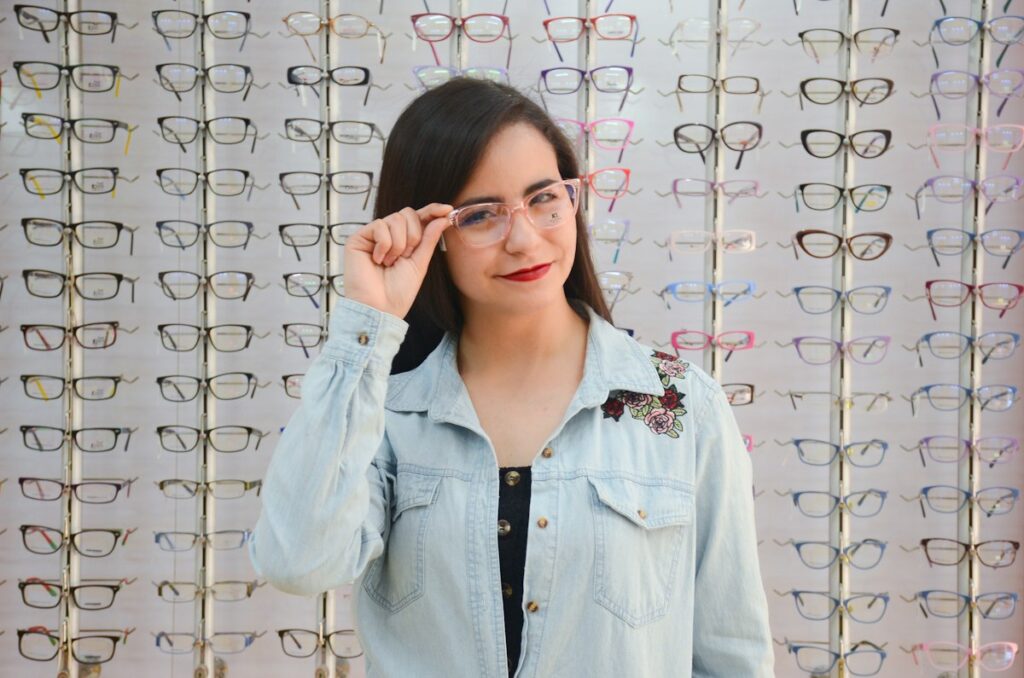 Woman trying on a pair of eyeglasses in front of a wall of frames in an optical store