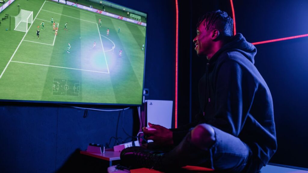 Junger Mann spielt ein Fußball-Videospiel in einem blau beleuchteten Raum