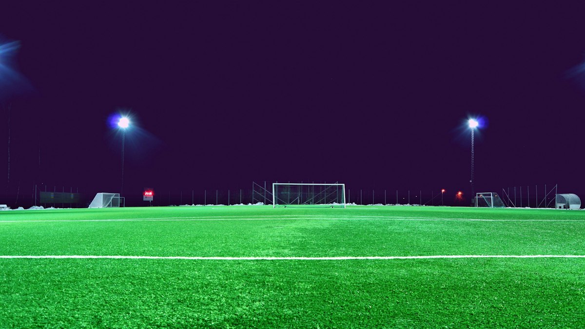 Grüner Fußballplatz unter Flutlicht bei Nacht