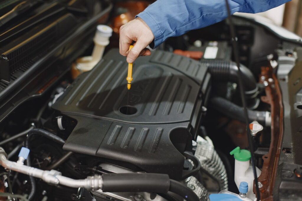 Gloved hand checking a car engine oil dipstick under the hood