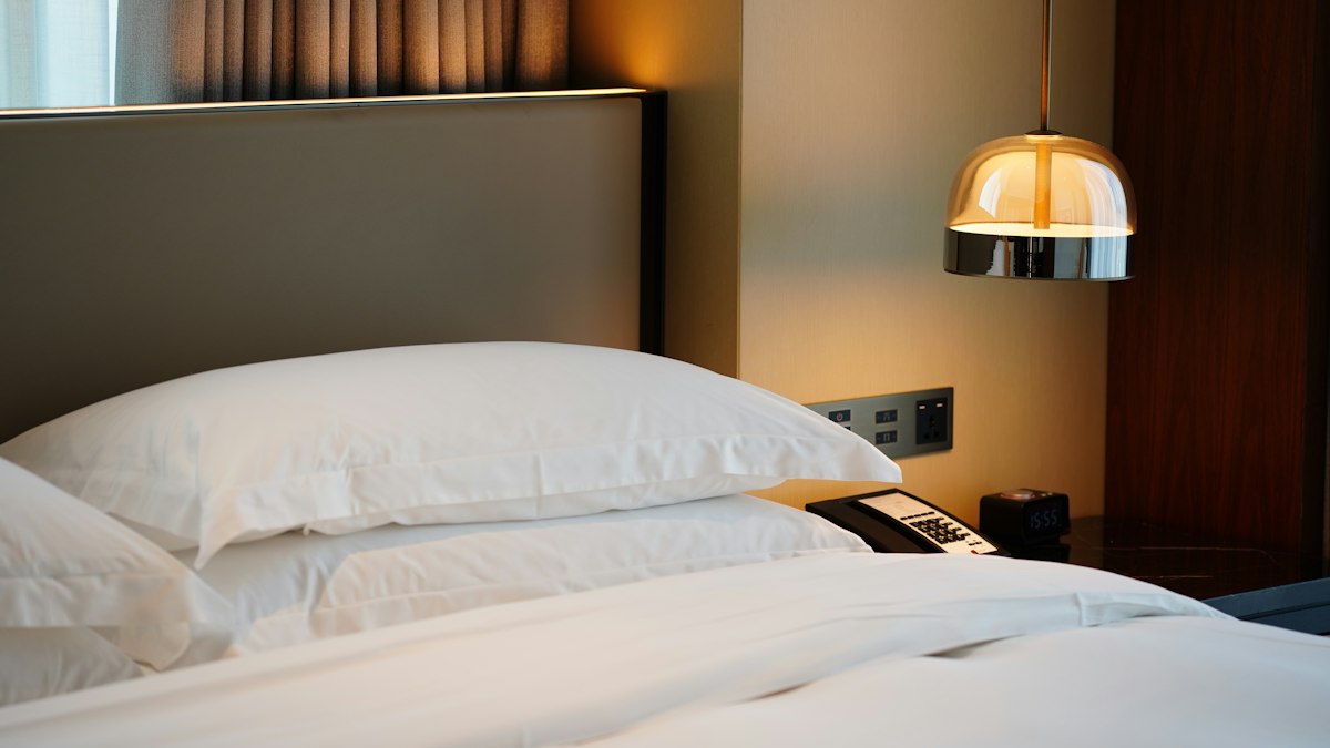 Close-up of a made hotel bed with crisp white pillows and a brass pendant lamp