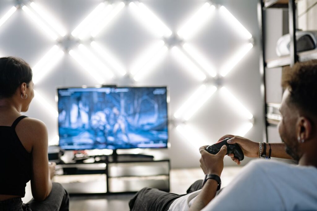 Two friends playing an action game on a large TV in a living room