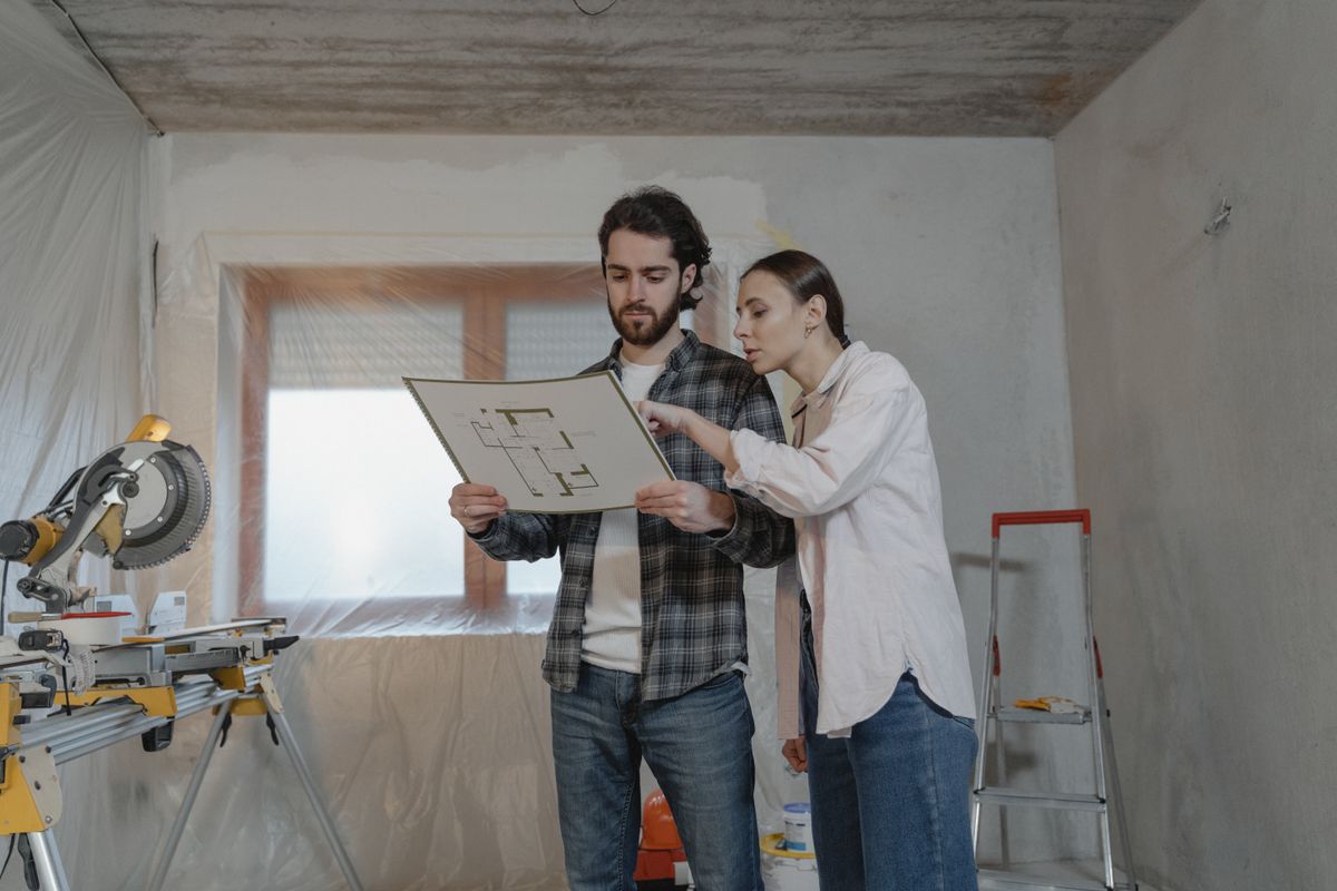 Couple reading a floor plan in a room under renovation
