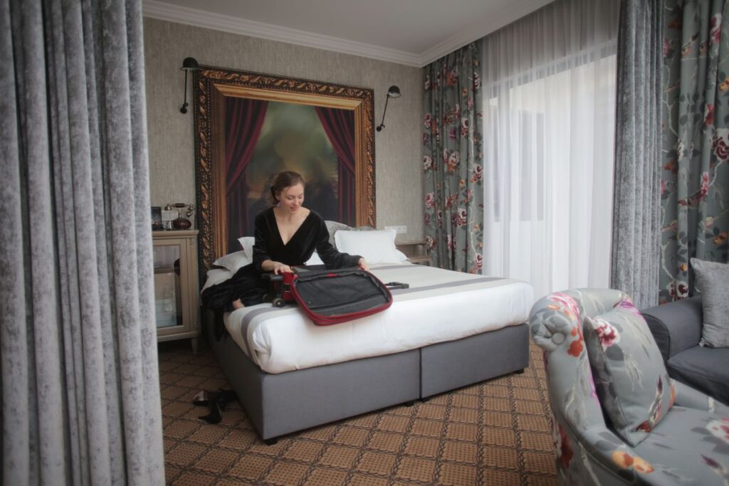 Traveler unpacking a suitcase on the bed of a bright hotel room