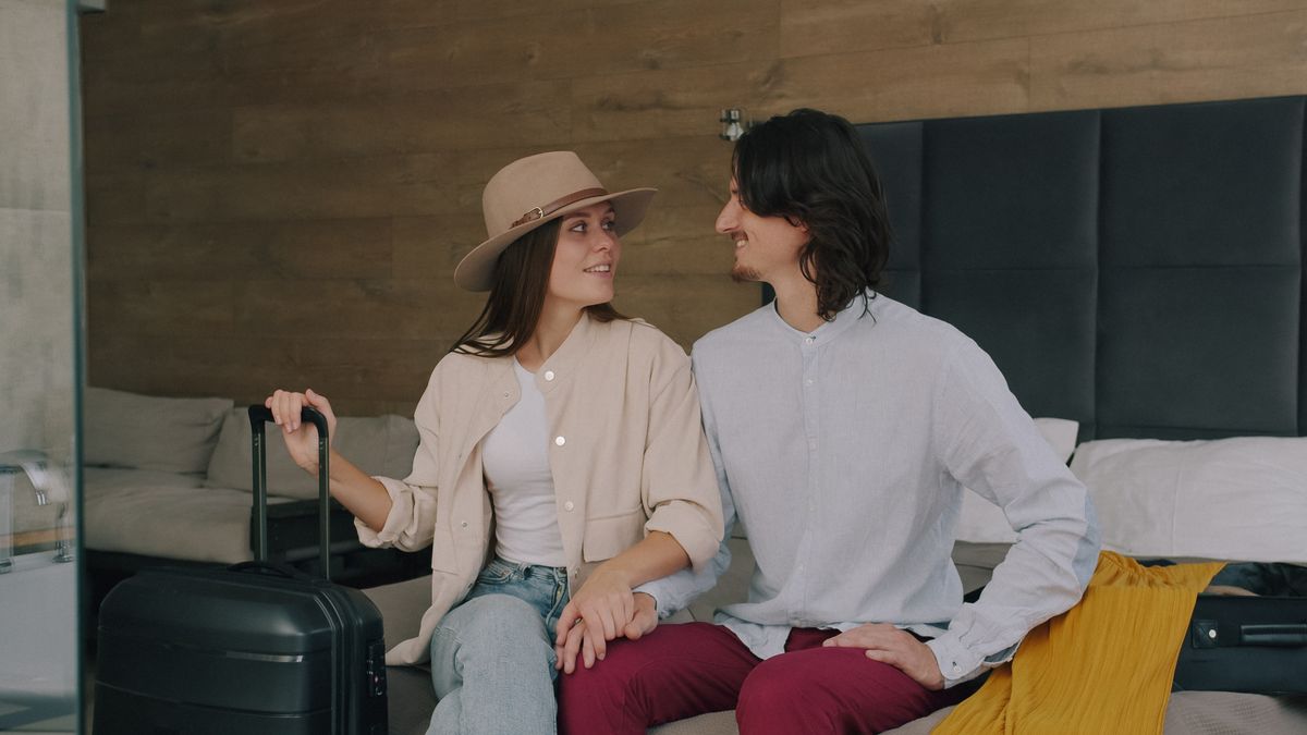 Couple sitting on a hotel bed beside their suitcase at the start of a trip