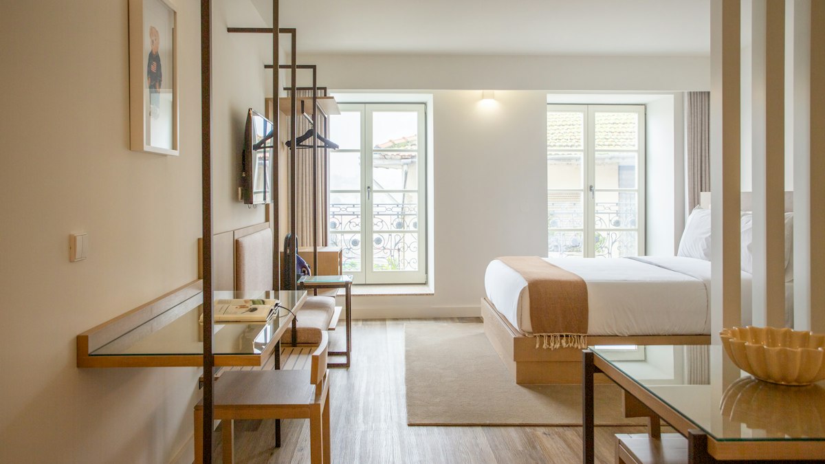 Ljust hotellrum med dubbelsäng, skrivbord och höga fönster