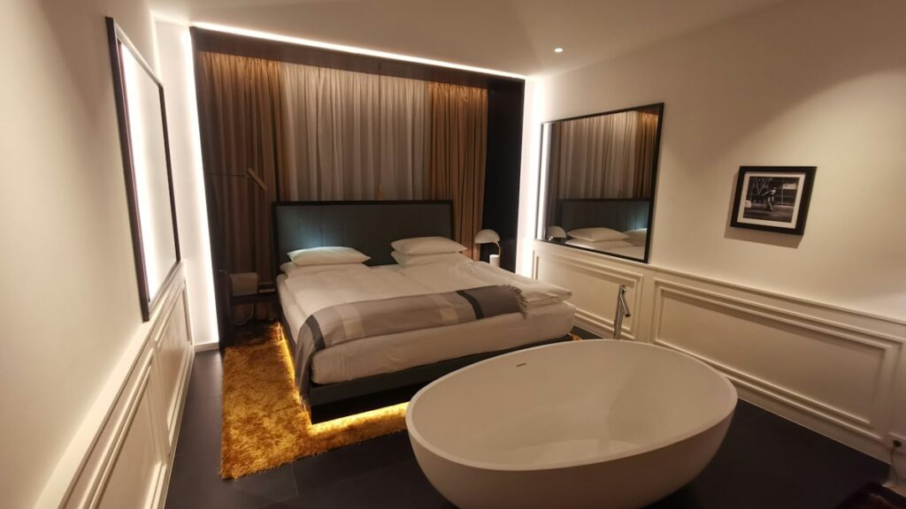 Elegant hotellrum med dubbelsäng och fristående badkar i varm belysning