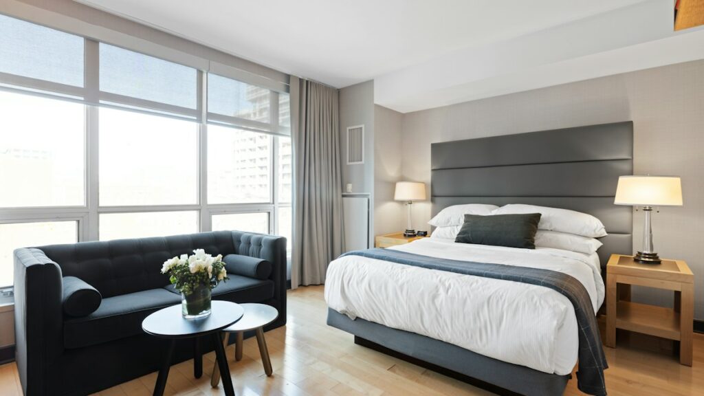 Ljust hotellrum med dubbelsäng, soffa och stora fönster