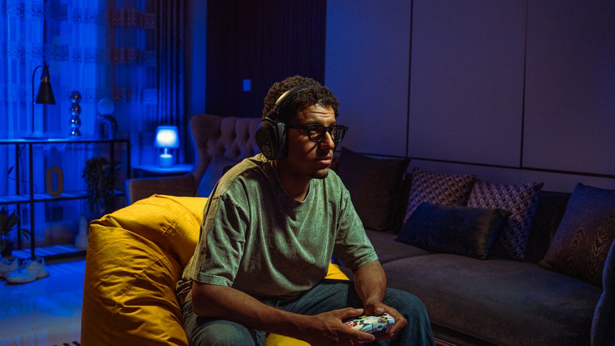 Gamer in headphones playing a console game in a blue-lit room