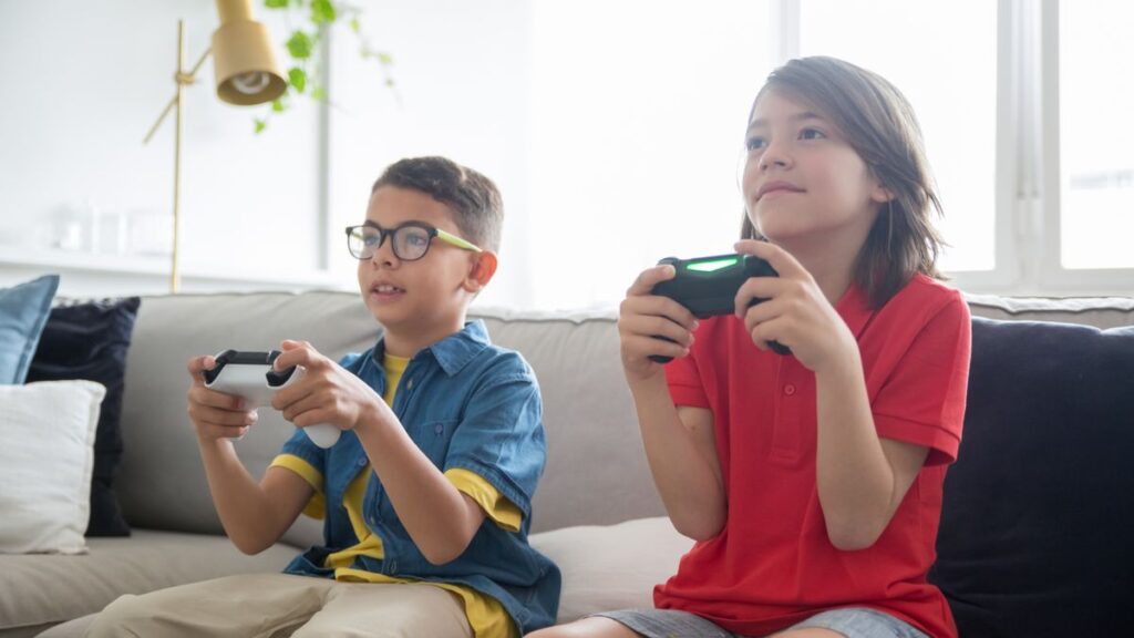 Two children playing video games together on a sofa