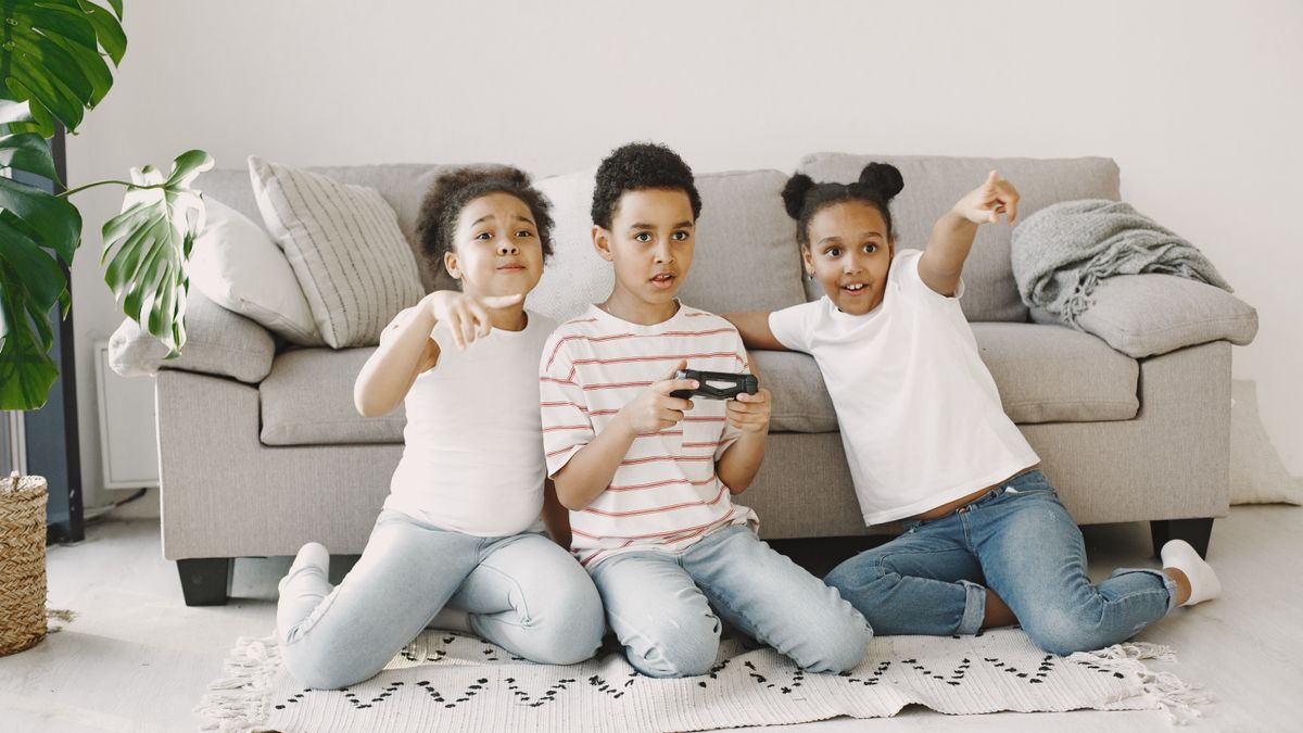 Three children playing a video game on a living room rug