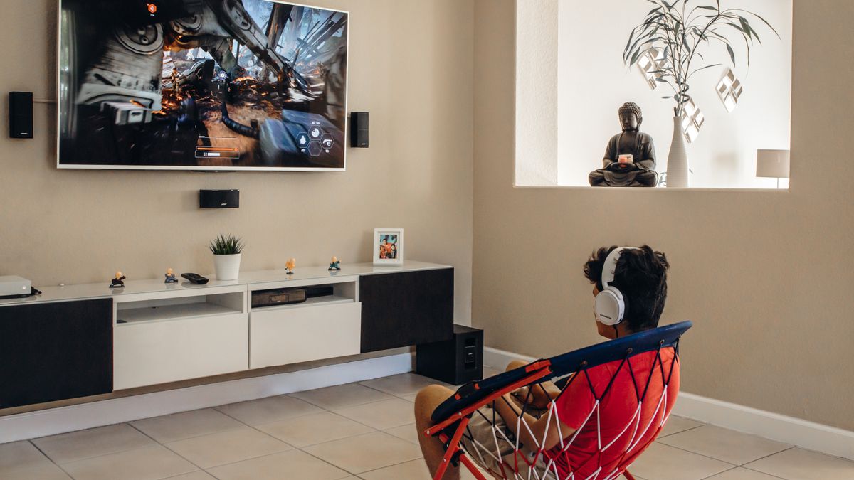 Gamer in headphones playing on a wall-mounted TV in a living room