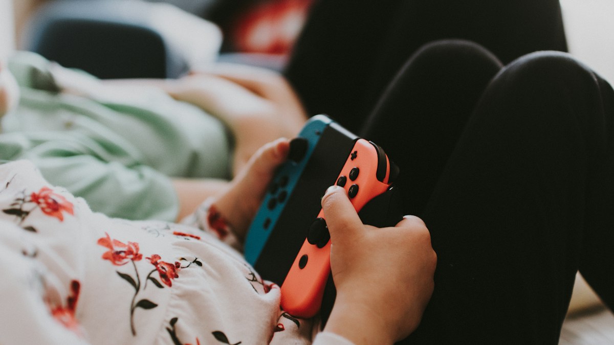 Hände halten eine Spielkonsole mit blauem und rotem Controller