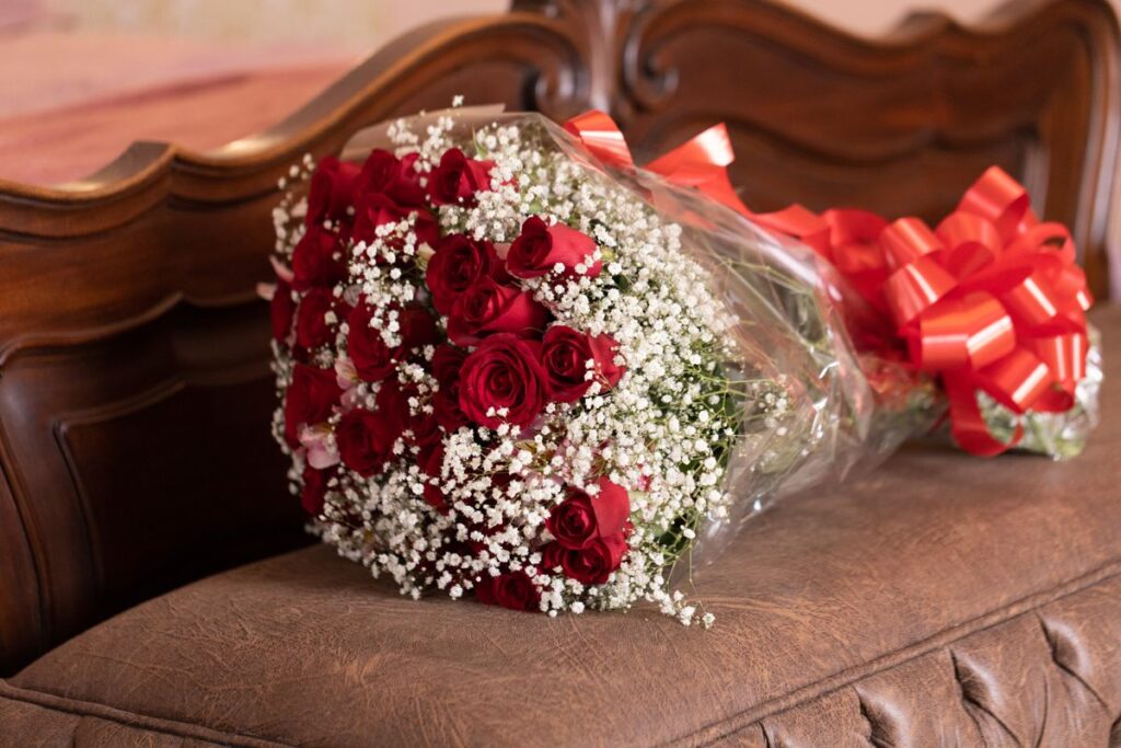 Large bouquet of red roses wrapped with a red ribbon bow on a wooden sofa