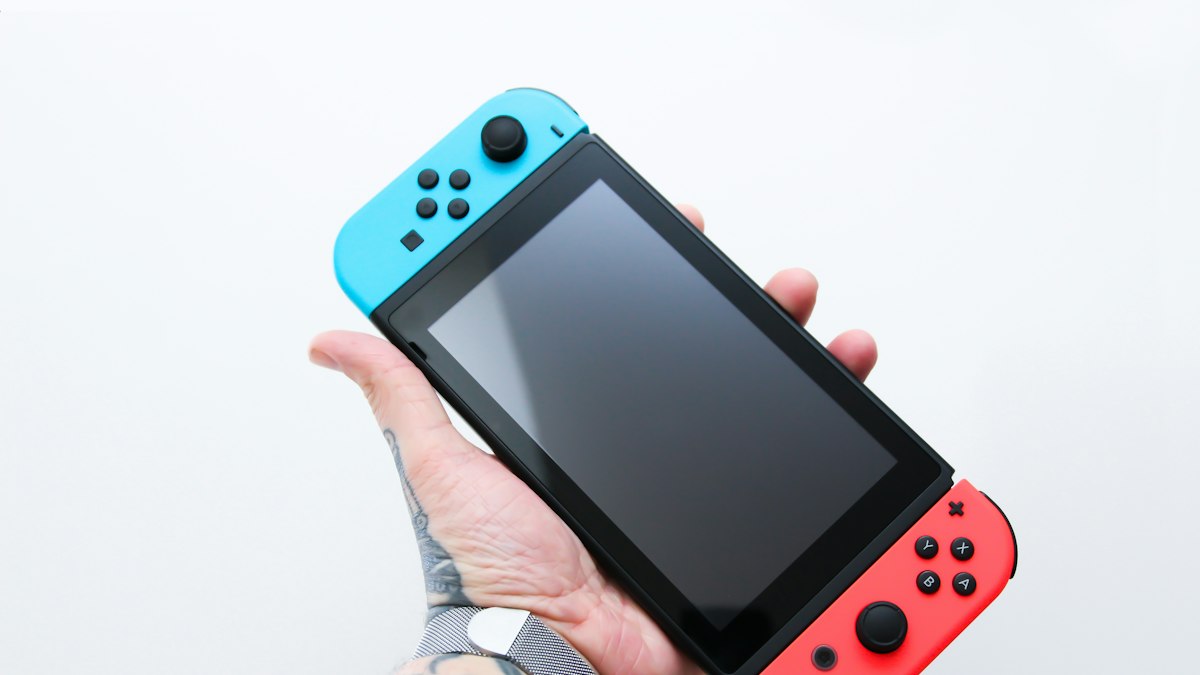 Hand holding a handheld games console with a blank screen