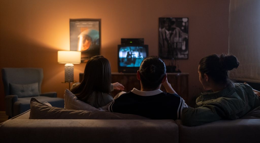 Three people watching a film on a television in a dark living room