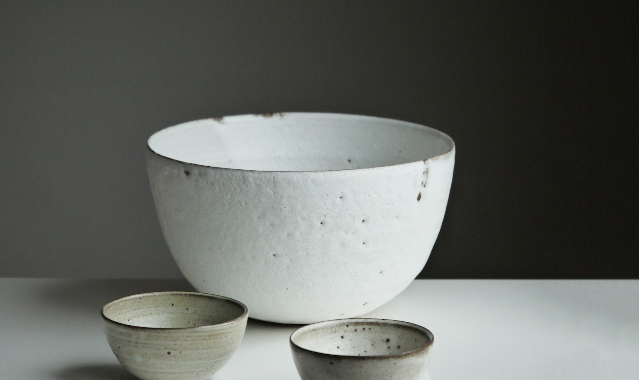 A large speckled serving bowl with two small bowls in front of it on a plain surface
