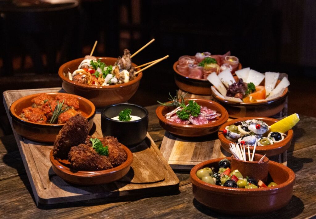Terracotta serving bowls of different sizes holding shared dishes, olives and dips on wooden boards