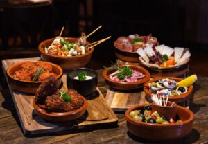 Terracotta serving bowls of different sizes holding shared dishes, olives and dips on wooden boards