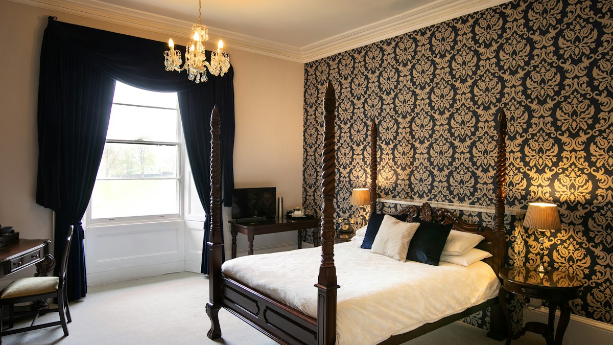Classic hotel room with a four-poster bed, damask wallpaper and a chandelier
