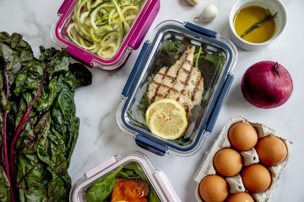 Grilled chicken and vegetables packed in clip-lid storage containers on a marble counter
