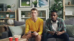 Two friends playing video games together on a sofa